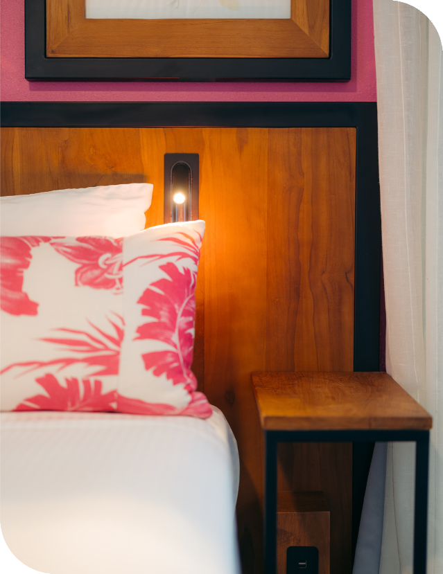 "Cozy bedside area in a room at Ilima Hotel, featuring a wooden nightstand with a lit lamp